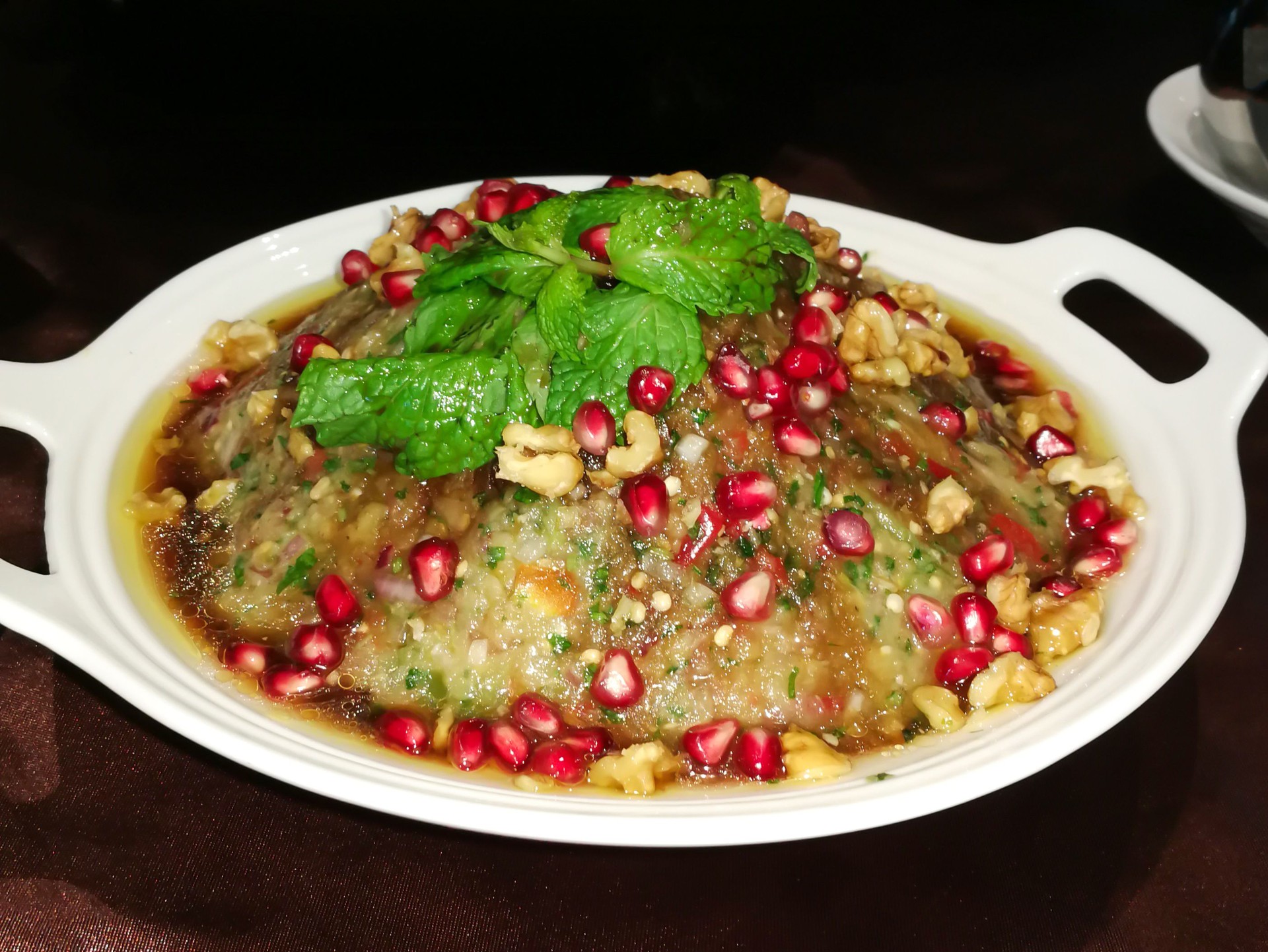 Baba Ghannouj creamy eggplant dip served in bowl topped with pomegranate seeds, walnuts, and fresh mint side view of gourmet Middle Eastern appetizer